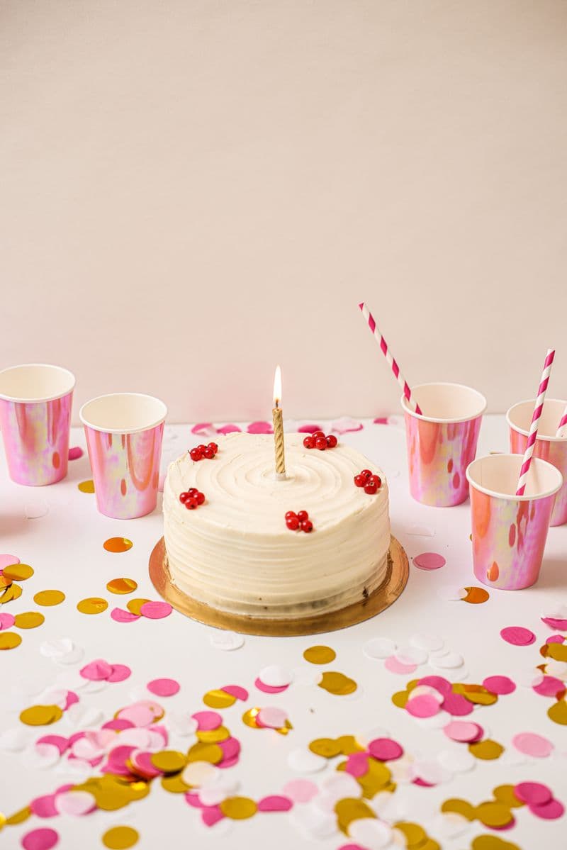 Torta de cumpleaños con una vela, entre confeti y vasos de colores